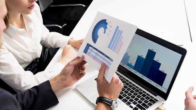 Two people reviewing charts on a laptop and printed report